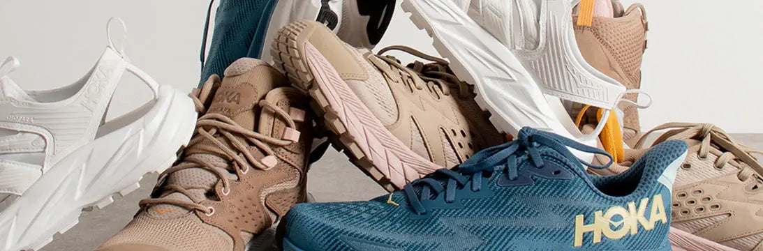 Assortment of Hoka trainers & running shoes in various colours, including tan, pink, and blue, showcasing thick soles and lightweight design.