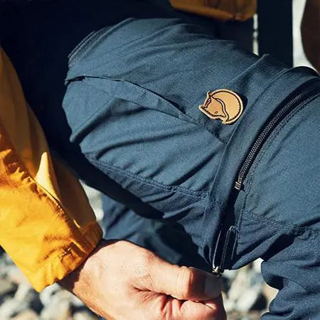 Navy blue Fjällräven walking trousers pocket with a yellow logo patch.