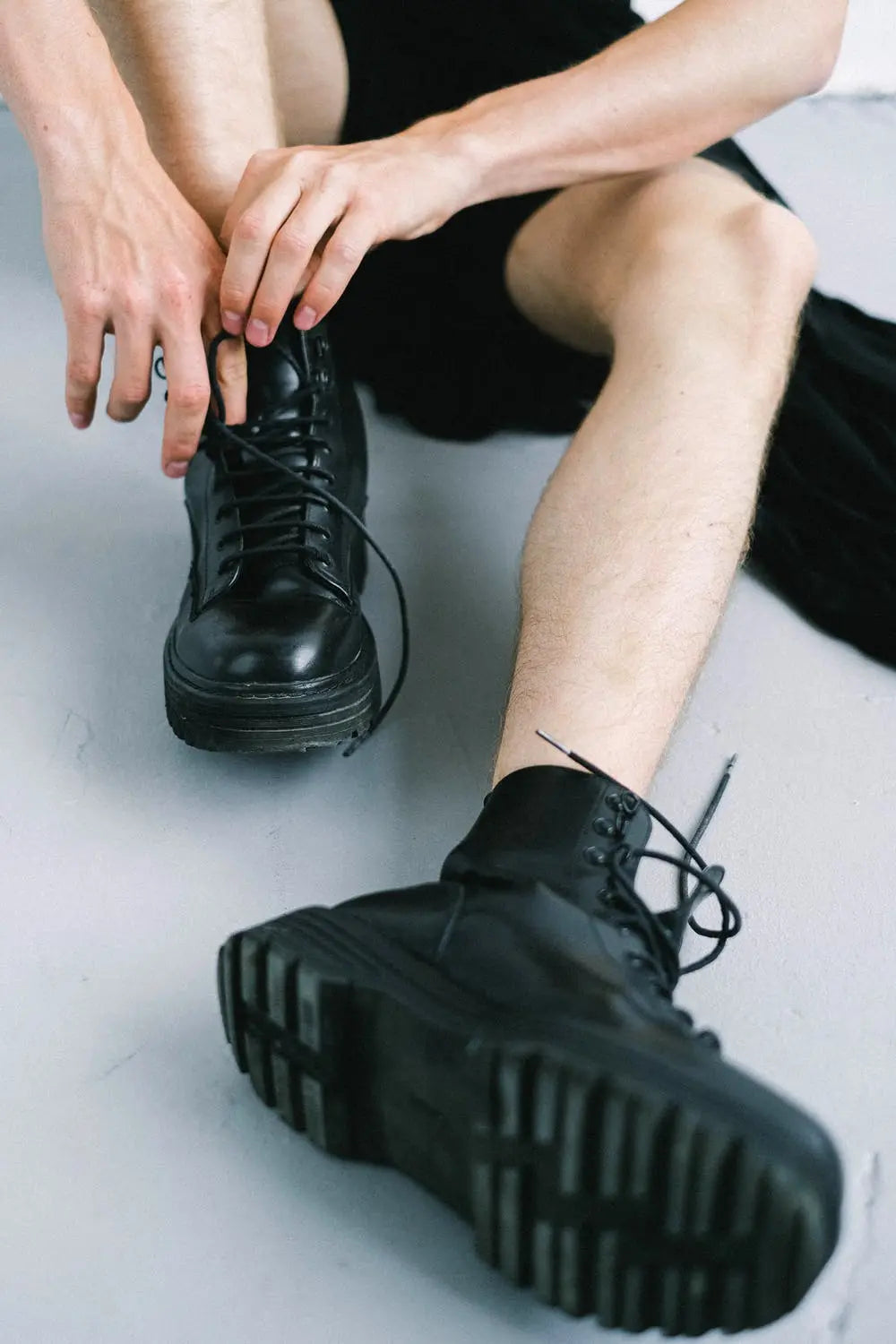 Person tieing the laces of chunky black boots with a thick treaded sole.