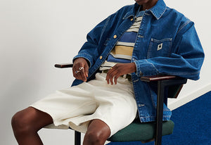 Man sitting on a chair wearing a denim jacket, striped t-shirt and Shorts