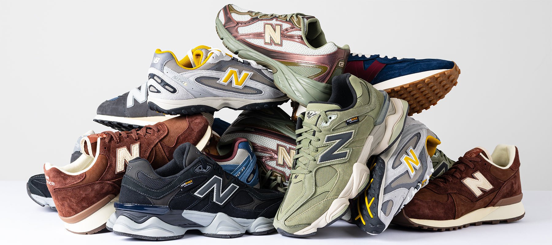Stacked selection of New Balance trainers in mixed colourways featuring suede and mesh uppers with cushioned soles.