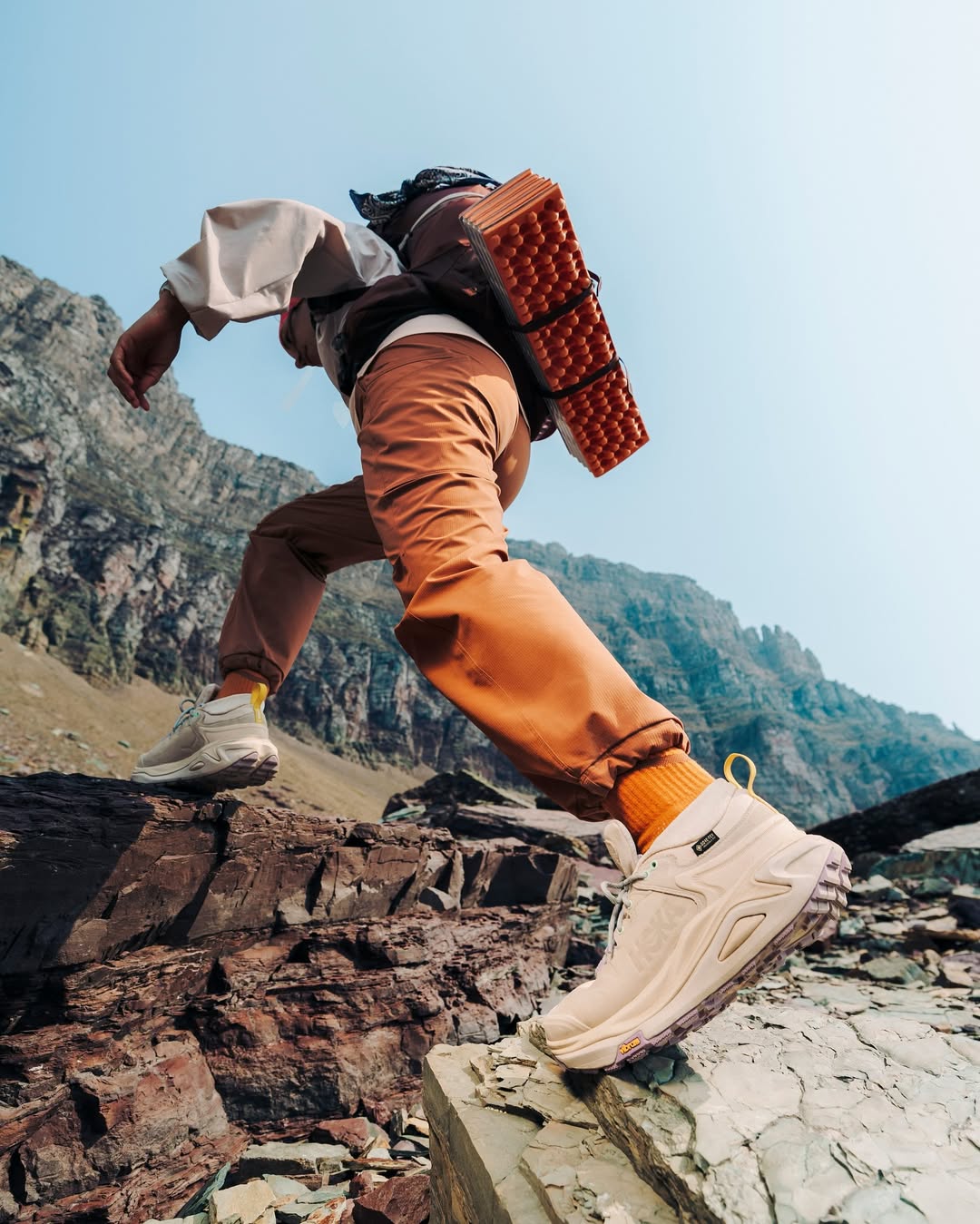 Man crossing rocky ground wearing HOKA trainers with cushioned soles and strong grip, designed for comfort and stability on uneven surfaces.