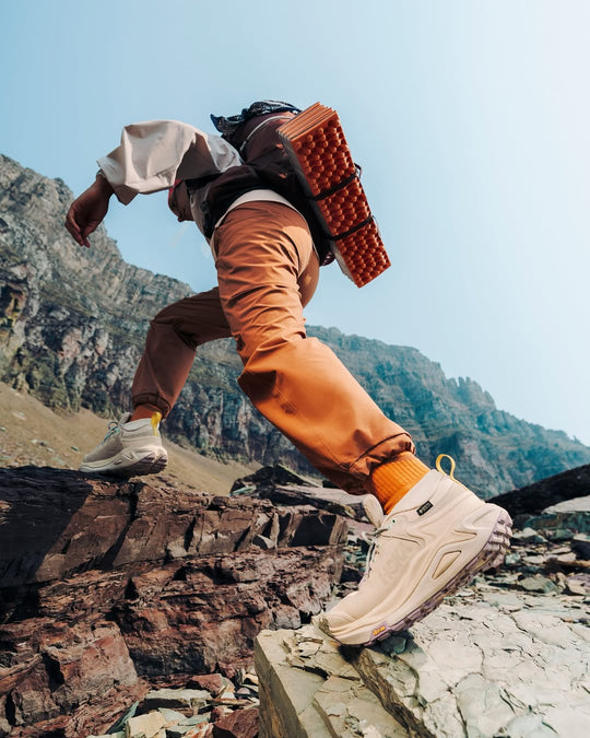 Man crossing rocky ground wearing HOKA trainers with cushioned soles and strong grip, designed for comfort and stability on uneven surfaces.