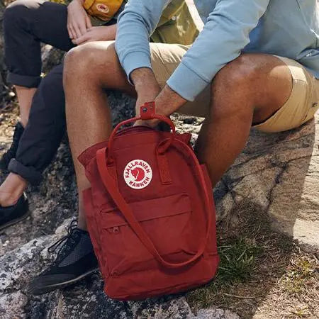Person sitting on a rock with a red Fjällräven Kånken backpack.