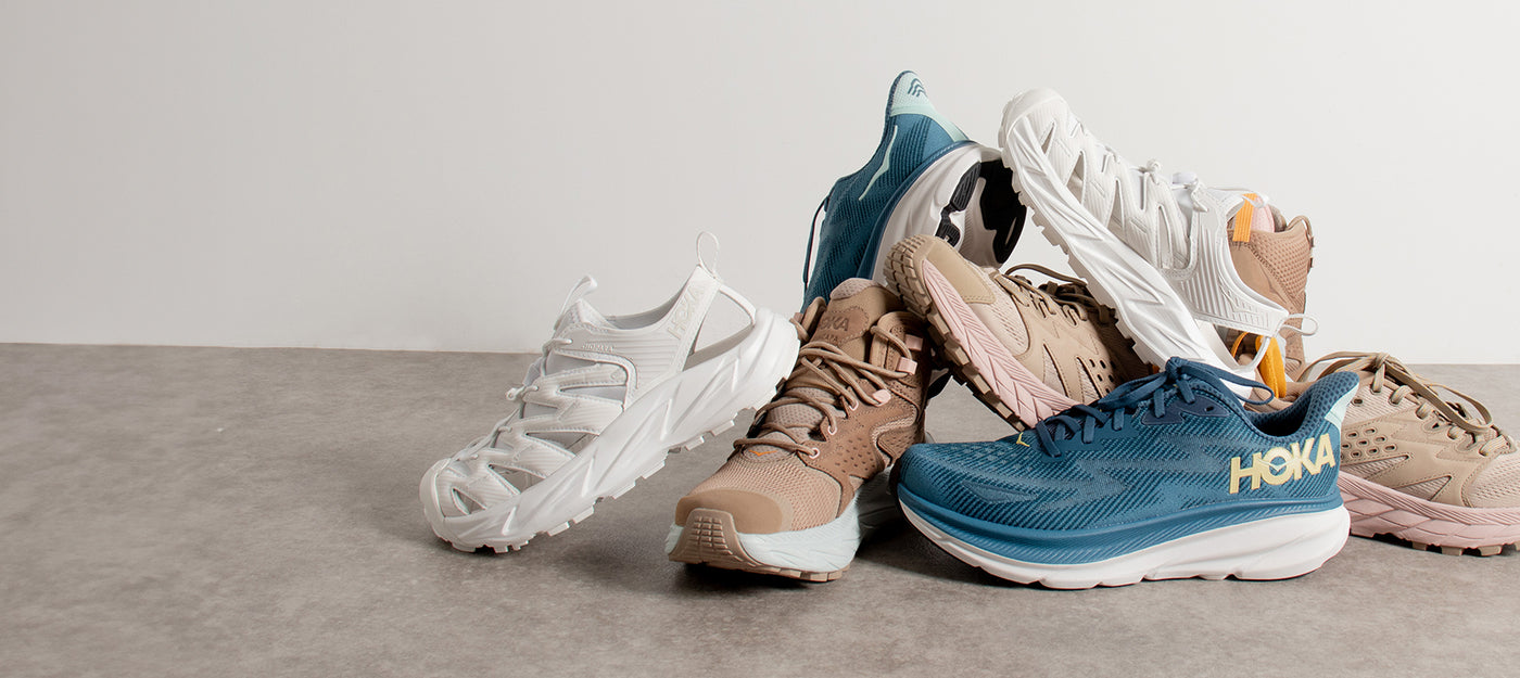 Selection of Hoka athletic shoes in shades of white, tan, and blue, showcasing the brand's cushioned running footwear with ergonomic design.