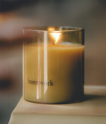 Candle in a glass jar labeled 'homework' on a wooden surface with a blurred background