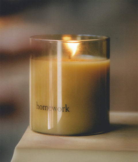 Candle in a glass jar labeled 'homework' on a wooden surface with a blurred background