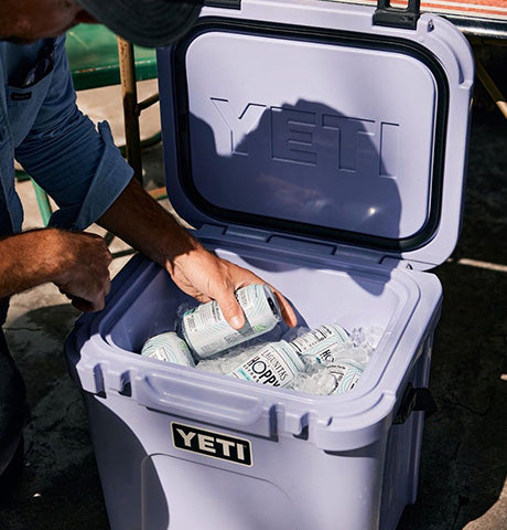 Person reaching into an open Yeti cooler filled with ice and canned drinks, showcasing the brand's effective insulation and cooling capabilities for outdoor activities.